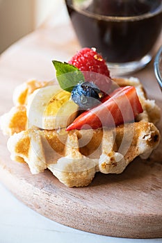 Close up of waffles with berries and honey on a wooden board