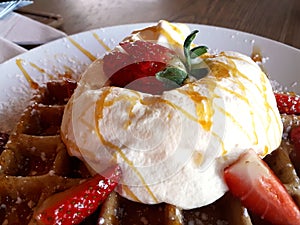 Close up waffles with cream and strawberries on white plate