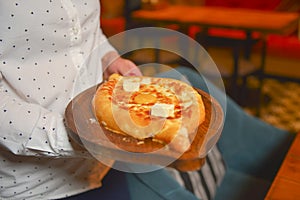 Close up of waiter serving a plate of Khachapuri - hachapuri in Adjarian. Waiter at work. Restaurant service.