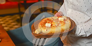 Close up of waiter serving a plate of Khachapuri - hachapuri in Adjarian. Waiter at work. Restaurant service