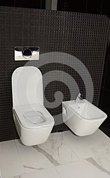 A close-up on wall-hung toilet and bidet set in a black mosaic tiled toilet room, bathroom