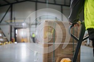 Close up of warehouse worker maneuvering pallet jack loaded with goods through the warehouse.