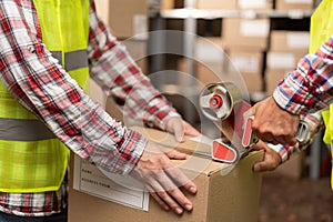 Close-up of warehouse workers preparing a shipment in a large warehouse, putting glue tape on boxes