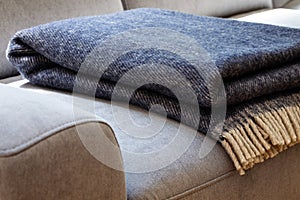 Close-up of a warm, navy blue, wool blanket with beige fringe on a comfy, gray sofa in a cozy living room interior