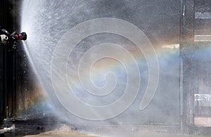 Close up water curtain from sprinkler of fire station with reflection of rainbow in front of area of fire occur