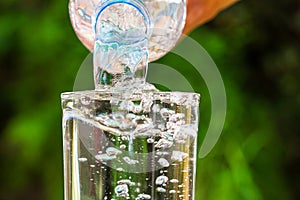 Close up of water flowing from drinking water bottle into glass on blurred green garden background