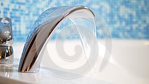 Close-up. water flows from a luxurious water tap into a large modern bathtub against a blue mosaic wall