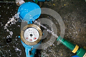 Close up water meter blue color. And a hose with flowing water.