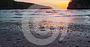 Close-up of waves spreading out over a beach at colorful yellow sunset. Sea crystal bay. Reflection of sun rays on water