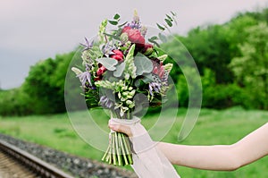 Close up of wedding bouquet with green, red and violet flowers and white ribbon. Bride with wedding bouquet in her hands.
