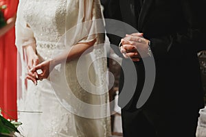 A close-up of wedding couple's hands while they pray in church