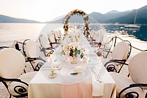 Close-up of a wedding dinner table reception. A table stands on beach overlooking mountains at sunset. Metal forged