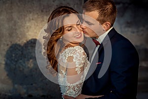 Close-up wedding portrait. The groom is tenderly kissing the charming happy ginger hair bride in the cheek.