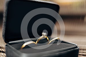 Close-up of wedding rings and an engagement ring with a large gem in a black velvet box against a blurred background.