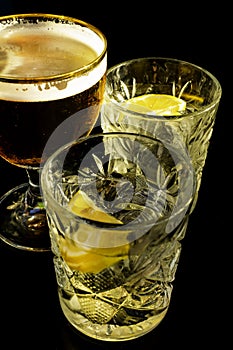Close up of a wet glass of cold light beer with foam and vermouth Martini alcohol cocktail with yellow lemon slice and ice cubes o