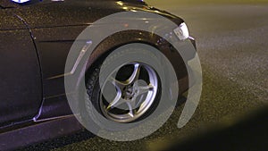 Close-up of wheel and body of shiny car. Action. Design coating of car with gold sequins sparkling in light of night