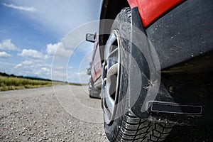 Close up of wheel of the car on dirt road at sunny spring day. View from the road