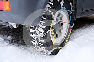 Close-up wheel of a gray car in colored iron chains on the snow, winter travel safety concept with snow chains on tire