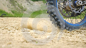 Close up wheel of powerful off-road motorcycle spinning and kicking up dry ground or dust. Professional motocross rider