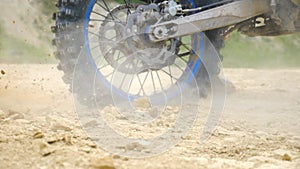 Close up wheel of powerful off-road motorcycle spinning and kicking up dry ground or dust. Professional motocross rider