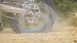 Close up wheel of powerful off-road motorcycle spinning and kicking up dry ground. Professional motocross rider starting