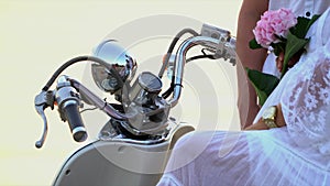 Close up of a wheel of the white moped. The woman with the man sit on the seashore. A big close-knit family have a rest