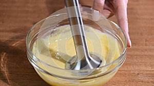 Close-up whipping homemade orange cream with a blender in a glass bowl.