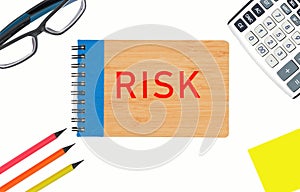 Close-up on a white background of a notebook with the inscription Risk, In the corners are glasses, calculator