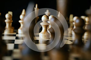 Close up of white and black chess pieces on board. Selective focus on first move of white pawn on chessboard. Concept of