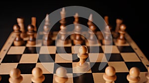 Close up of white and black chess pieces on board. Selective focus on first move of white pawn on chessboard. Concept of