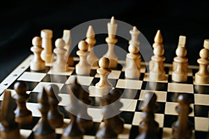 Close up of white and black chess pieces on board. Selective focus on first move of white pawn on chessboard. Concept of