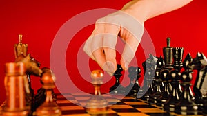 Close up of white and black wooden chess pieces on board. Man's hand makes move of black pawn on chessboard on a red