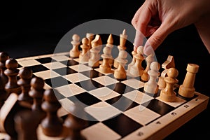 Close up of white and black wooden chess pieces on board. Woman's hand makes first move of white pawn on chessboard