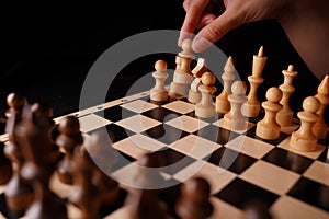 Close up of white and black wooden chess pieces on board. Woman's hand makes first move of white pawn on chessboard