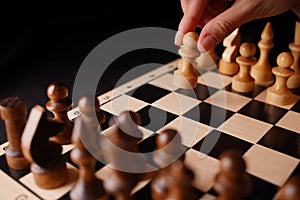 Close up of white and black wooden chess pieces on board. Woman's hand makes first move of white pawn on chessboard