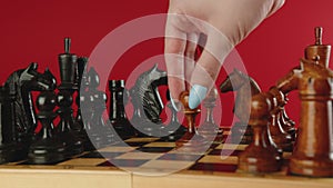 Close up of white and black wooden chess pieces on board. Woman's hand makes move of white pawn on chessboard. Concept