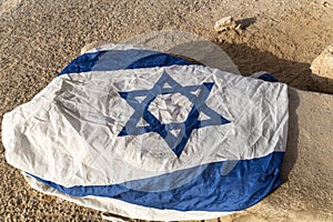 Close up of white and blue flag with David's star left on the ground in arid place. Symbol of promised land. Patriotic feelings.