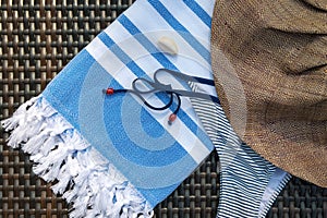 Close-up of a white and blue Turkish peshtemal / towel, bikini, white seashells and straw hat on a rattan lounger.