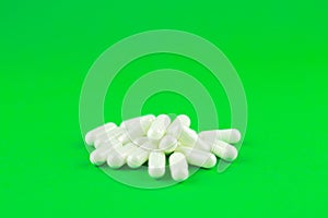 Close up white capsules on lime green background with copy space. Focus on foreground, soft bokeh. Pharmacy drugstore concept