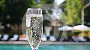 Close-up white champagne or prosecco glass against poolside at luxury resort hotel during vacation. Sparkling wine with