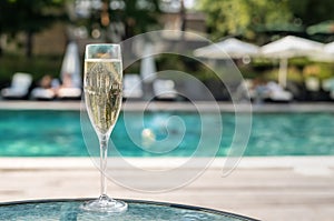 Close-up white champagne or prosecco glass against poolside at luxury resort hotel during vacation. Sparkling wine with