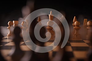 Close up of white chess pieces on board with dissipating steam. Two rows of wooden figures on chessboard on black