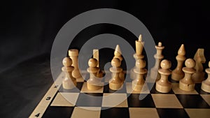 Close up of white chess pieces on board with dissipating steam. Two rows of wooden figures on chessboard on black