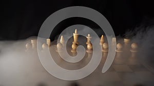 Close up of white chess pieces on board with dissipating steam. Two rows of wooden figures on chessboard on black