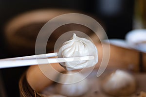 Close up white chopsticks holding dim sum Ha gow over wooden basket