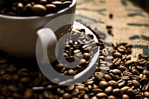 Close up of a white coffee cup full of coffee beans, surrounded