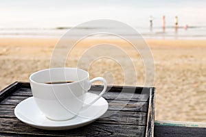 Close up white coffee cup on wood table at sunrise sand beach in the morning