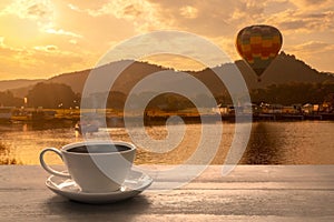 Close up white coffee cup on wood table and view of sunset in nature background