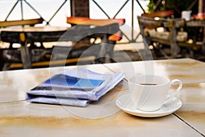 Close up white coffee cup on yellow table at sunrise sand beach with newspaper in the morning