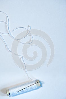 Close-up of a white color thread spool of the sewing machine with a needle, diagonally placed against a white background